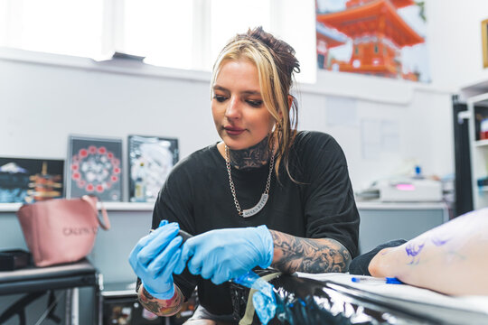 a young tattoo artist girl preparing a tattoo machine to start drawing, medium shot, tattoo salon. High quality photo