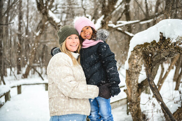 attractive mother with cute child daughter in winter forest