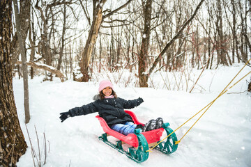 attractive American mother with cute child daughter in winter forest in sled