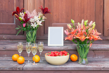 Lilies,  champagne, white frame, strawberry and oranges on steps of rustic wooden ladder. View with copy space.