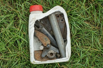 cut old used plastic dirty canister small white with engine oil under machine oil with various small iron parts for a motorcycle lies on green grass outdoors in summer