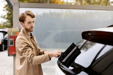 Portrait of positive man washing his car with window scraper at self-service car wash station