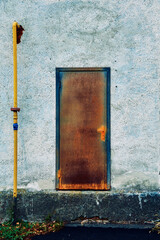 An old, rusty metal door at the entrance to the building, a yellow gas pipe runs along the wall, an unusual location of the door on the facade of the building