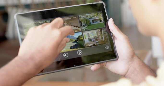 Hands of biracial man using tablet with home security camera views on screen, slow motion