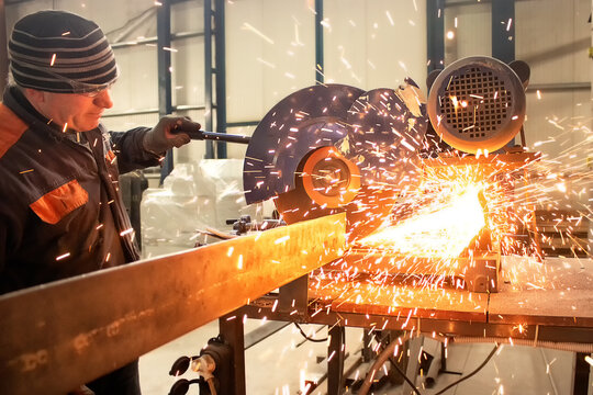 a welder, a white man, in a locksmith shop, on a large and noisy machine, cuts metal according to a drawing, long and hot sparks fly in all directions, the work is boiling - Powered by Adobe