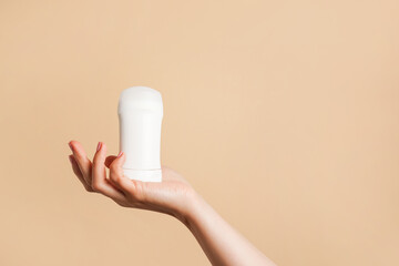 Female hand holds white body deodorant on beige background, copy space