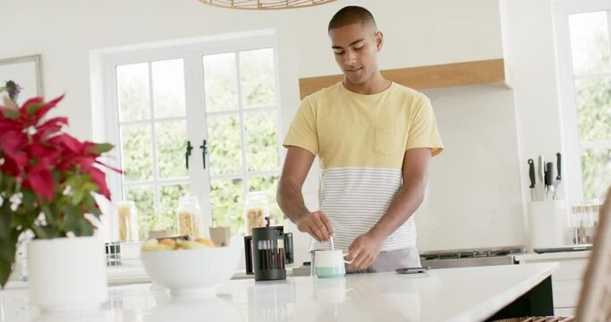 Happy biracial man making coffee in bright kitchen, slow motion
