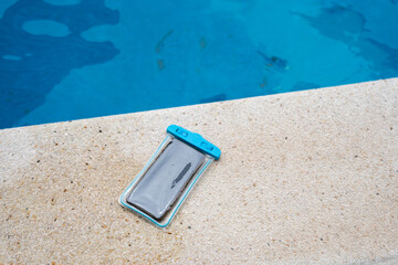 Waterproof case with a smartphone on the background of the pool on a sunny summer day.