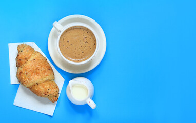 Cappuccino, cereal croissant and milk jug. Coffee and croissant on a blue background. The concept of healthy eating and sweet food. French breakfast. Flat lay, top view. Copy space