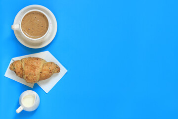Cappuccino, cereal croissant and milk jug. Coffee and croissant on a blue background. The concept of healthy eating and sweet food. French breakfast. Flat lay, top view. Copy space