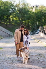 Young man and woman walking with gorgeous australian collie in urban area. Happy couple with their pet in the city, taking dog downtown