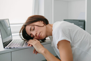Woman sleeping on laptop keyboard. Tired, frustrated, exhausted, stressed woman sitting at desk working on laptop. Daylight work. 
