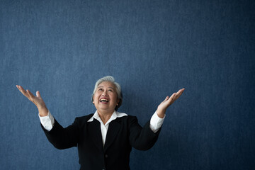Portrait of middle aged business woman standing isolated on blue background and raise your arms to show success, looking at the camera with smile, Successful businesswoman, ceo, director, manager