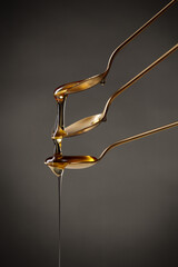 Golden spoons with pouring honey on a dark background. Honey overflowing from spoon to spoon.