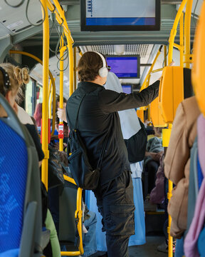Authentic multicultural passengers of different ages at rush hour ride inside public transport, a man with white wireless headphones in a modern bus, public electric transport in Krakow.