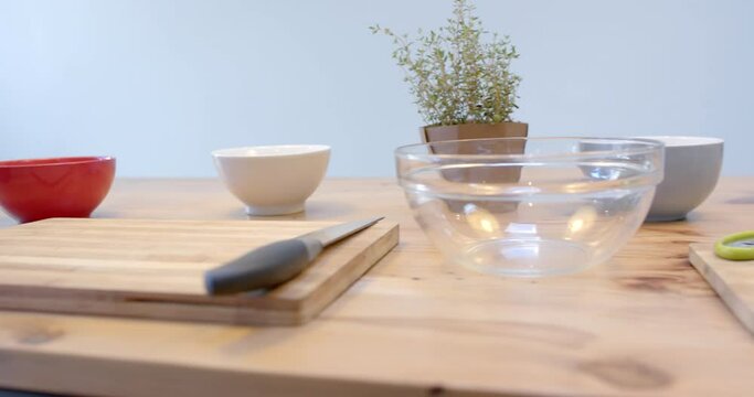 Close up of bowls, cutting boards and knife on wooden table in kitchen, slow motion