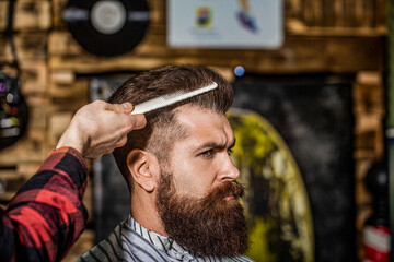 Hairdresser does styling with a comb in barbershop. Bearded man in barber shop. Work in the barber...