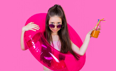 Kid girl in glasses holds a cocktail, rubber circle for swimming in sea on pink background. Child girl to swim in sea holding rubber circles. Happy girl in sunglasses holding rubber circle, swimsuit