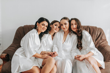 The bridesmaids are looking at the camera together with the bride. The bride and her fun friends are celebrating a bachelorette party in matching dresses. Bride and friends in the room