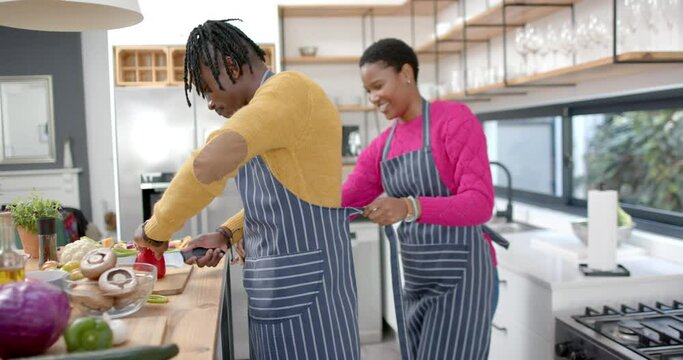 Happy african american couple in aprons preparing meal in kitchen, slow motion