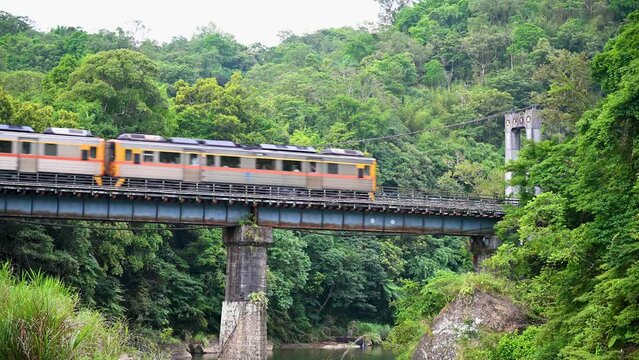 A yellow diesel train passes the bridge over the valley. Along the Pingxi line, there are river valleys, potholes and waterfalls. Taiwan