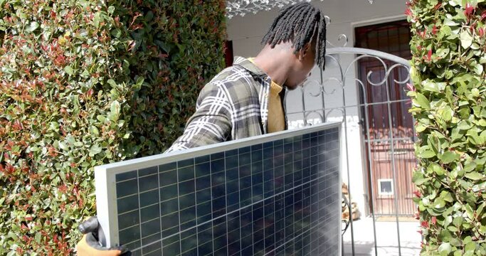 African american man holding photovoltaic panel entering property, slow motion