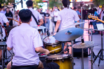 Selective focus to drum set and boy drummer with blurry teen group music band and concert audience. Street music concert background.