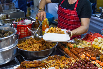 Vietnamese woman serving chicken paws in plastic box with chili in vietnamese night market