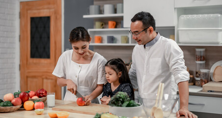 The family members happily and playfully prepare a bowl of various types of fruity and vegetable salad. Making quirky faces, joking, laughing, smiling, can create a good mood and positive atmosphere.