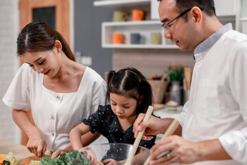 The family members happily and playfully prepare a bowl of various types of fruity and vegetable salad. Making quirky faces, joking, laughing, smiling, can create a good mood and positive atmosphere.