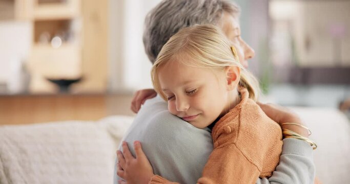 Love, sweet and grandmother hug her grandchild while relaxing in the living room of a home. Happy, smile and senior woman embracing a little girl kid with care on sofa in the lounge at her house.