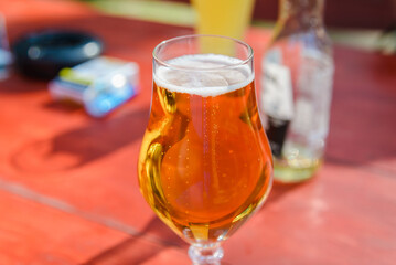 Glass of light beer on the wooden table.Glass of beer in nature.Empty bottle,a packet of cigarettes in a blurred background,summer day.