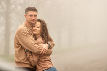 young heterosexual couple, white race, on a foggy day on the street, a young man embraces his young woman, a young woman smiles, a moment of joy, love