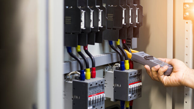 Electrician engineer work tester measuring voltage and current of power electric line in electical cabinet control.	