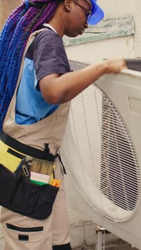 Vertical video Proficient worker starting comission on defective air conditioner, meticulously disassembling condenser metal front coil panel. Capable electrician dismantling hvac system to check for