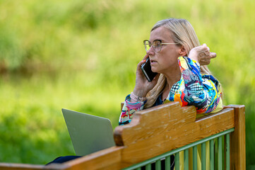 middle age woman at the garden working from home using laptop and speaking on the phone