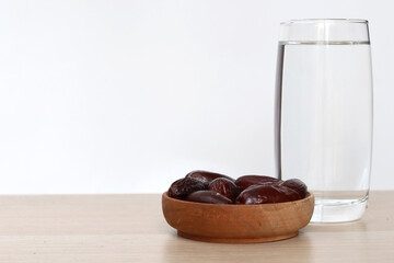 Glass of water with a bowl of date fruit on a wooden table and white background. Muslims break the fast with water and dates fruit