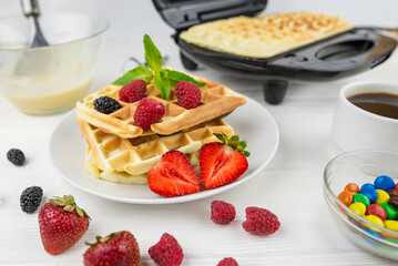 Belgian waffles with different berries on white.