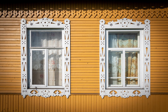 Deux fen&ecirc;tres encadr&eacute;es avec des chambranles en bois sculpt&eacute; orn&eacute;s de motifs traditionnels blancs &agrave; l'ext&eacute;rieur d'une isba russe, maison construite en bois situ&eacute;e dans le nord de la Russie