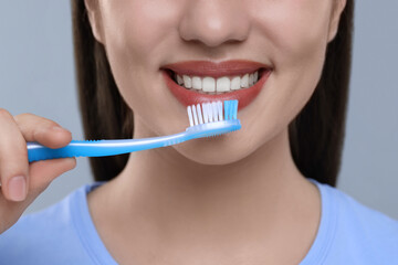 Woman brushing her teeth with plastic toothbrush on light grey background, closeup