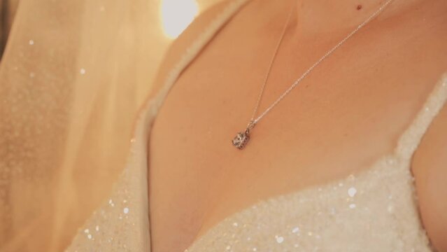 The girl hand straightens the necklace. The bride hand straightens the necklace. Bride dresses a necklace. A young woman puts on a chain with a pendant around her neck. Girl dresses a necklace.