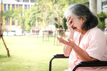 Fototapeta premium An elderly Asian female patient sits in a wheelchair in a hospital, she regrets her illness. Elderly disease concept, health insurance. copy space