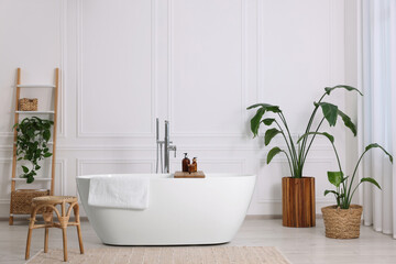 Fototapeta na wymiar Stylish bathroom interior with beautiful tub, stool and houseplants