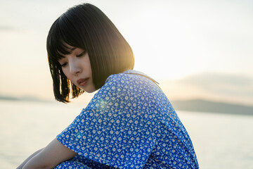 夕暮れの海にいる青いワンピースの女性