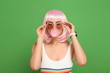 Beautiful woman in sunglasses blowing bubble gum on green background