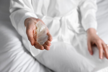 Woman holding unrolled condom on bed, closeup. Safe sex