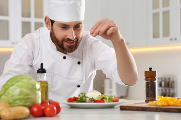 Professional chef salting delicious salad at marble table in kitchen