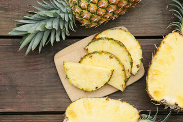 Cut and whole ripe pineapples on wooden table, flat lay
