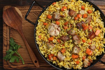 Delicious pilaf with meat, carrot and garlic served on wooden table, top view
