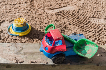Red and blue toy truck carrying green shovel against sand pit in background, leisure and lifestyle concept illustration.